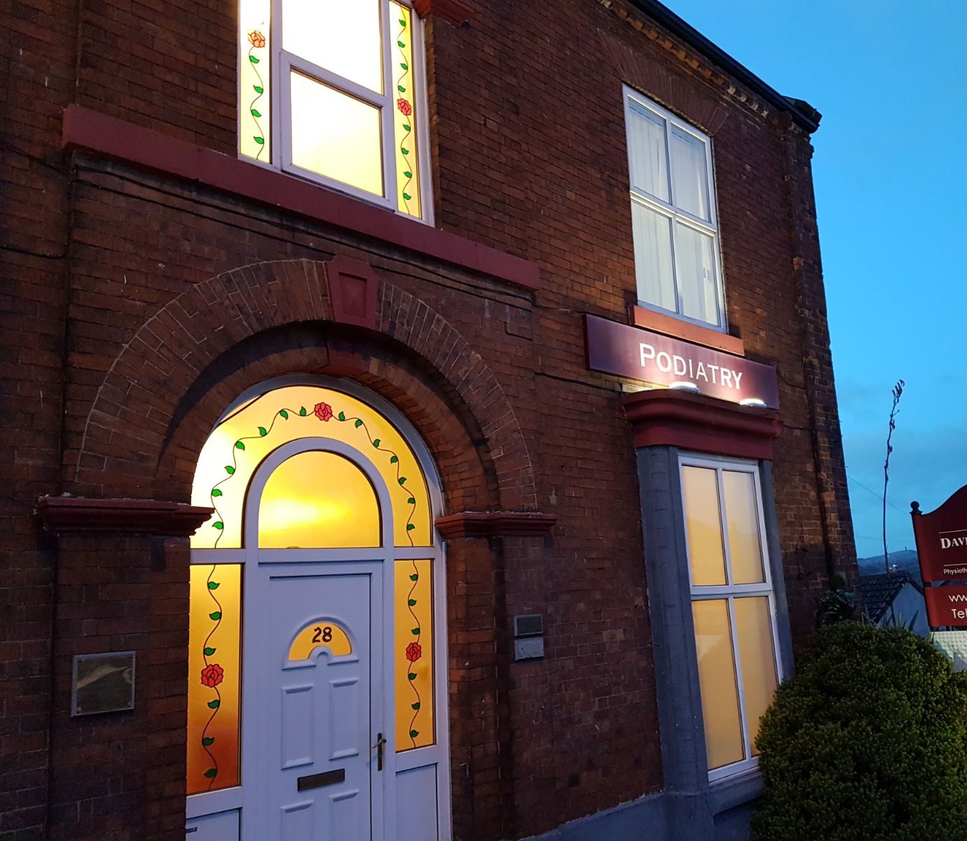 The lit front door of No. 28 Cheetham Hill Road at dusk, with stained glass and the number 28